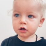 Close-up of a young blonde child with wide blue eyes, looking outward with curiosity; symbolising the emotional legacy passed down through presence, tone, and nervous system cues.