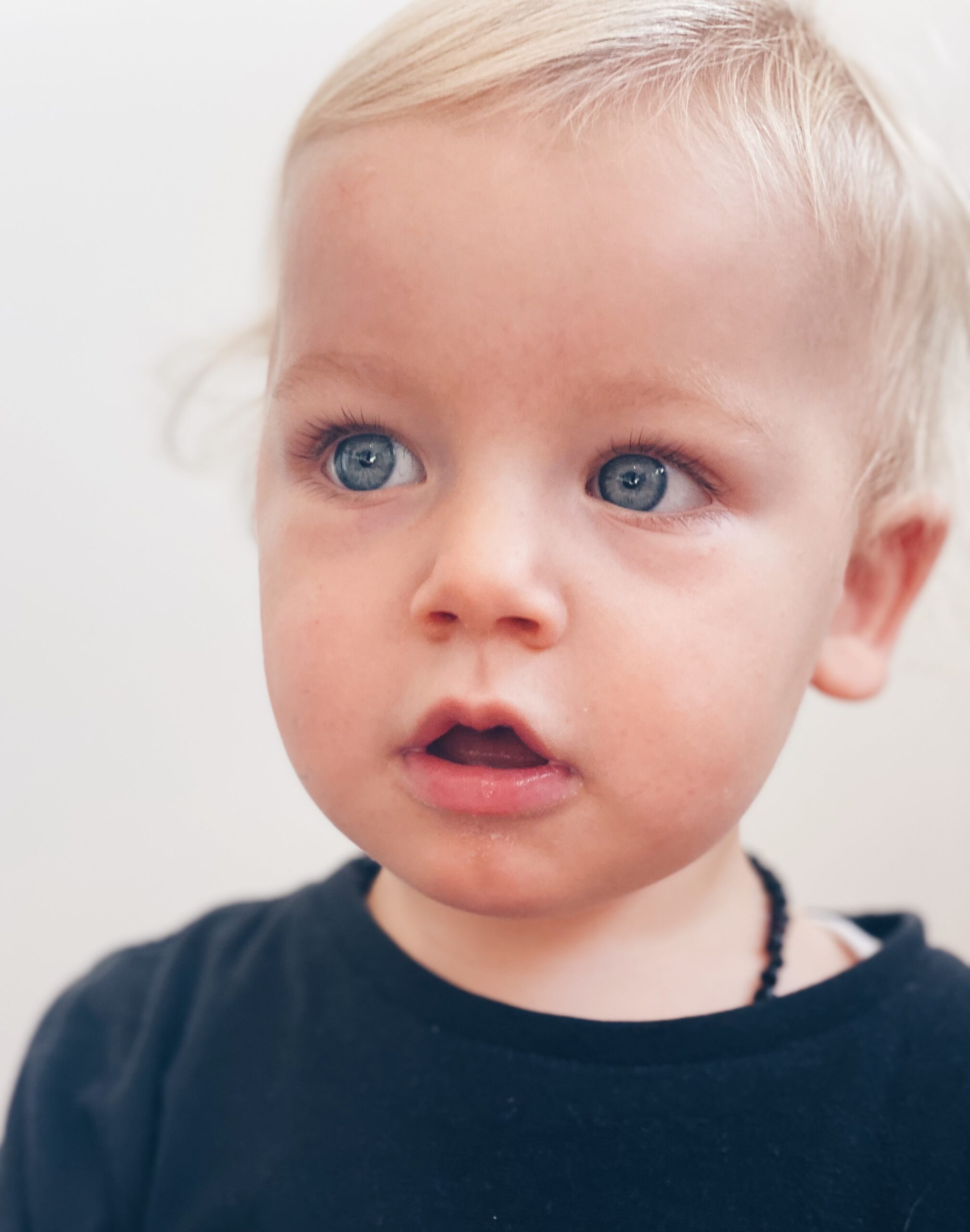 Close-up of a young blonde child with wide blue eyes, looking outward with curiosity; symbolising the emotional legacy passed down through presence, tone, and nervous system cues.